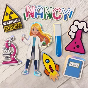 May include: A collection of science-themed stickers including a yellow radiation warning sign, the name NANCY in colourful letters, a scientist in a lab coat, a pink microscope, a blue test tube, a pink flask with bubbles, a rocket, and a science notebook.
