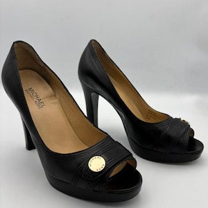 May include: A pair of black leather peep-toe platform heels with a gold buckle detail. The heels are about 4 inches tall and have a platform of about 1 inch. The shoes are labeled "MICHAEL MICHAEL KORS".