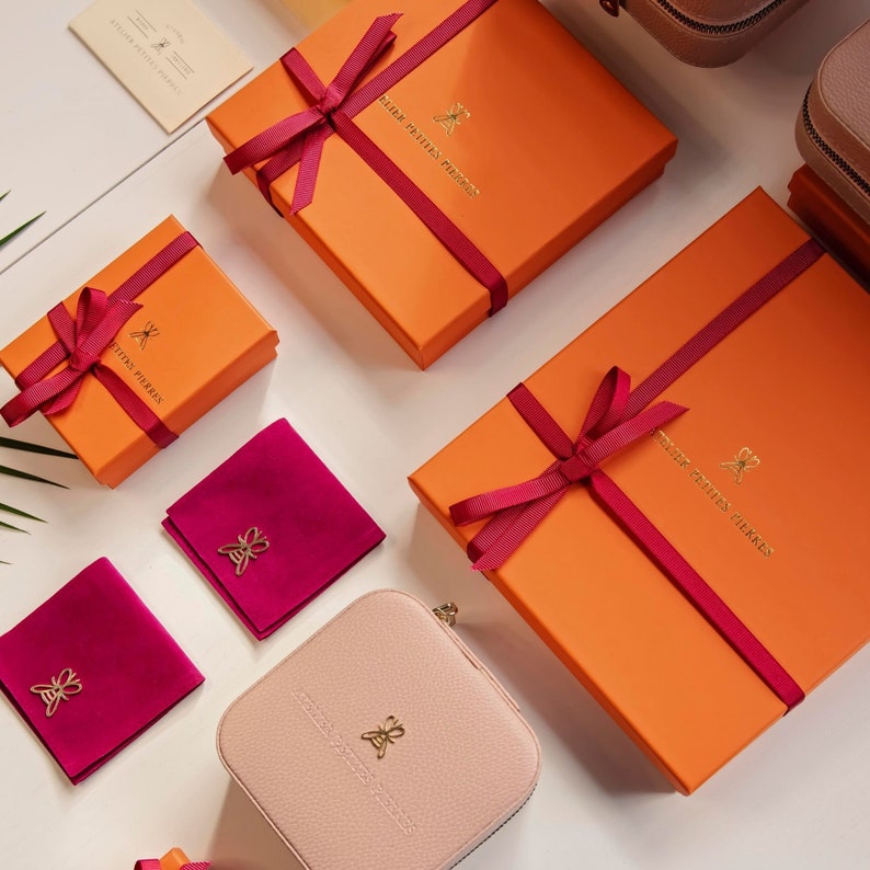 May include: Assortment of gift boxes with red ribbon bows and a butterfly logo. The boxes are orange and pink with the text "Petite Pierres" and "Fleur Petite Pierres".