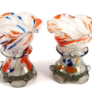 Peut inclure: Deux vases en verre transparent avec un motif en spirale orange, bleu et blanc. Les vases ont un sommet festonné et une base grise avec un motif décoratif.