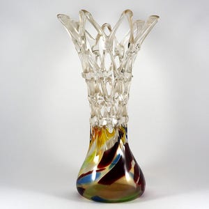 Peut inclure: Un vase en verre transparent avec un design unique et complexe. Le vase a un sommet large et ouvert et une base étroite. Le fond du vase est décoré de tourbillons de verre abstraits et colorés dans des tons de jaune, vert, bleu et rouge.