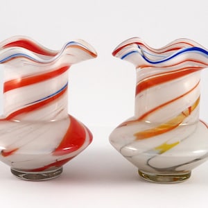 Peut inclure: Deux vases en verre blanc avec un motif en spirale de rouge, bleu et jaune. Les vases ont un sommet festonné et une base large.