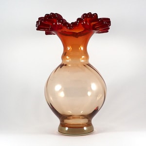 Könnte beinhalten: Eine klare Glasvase mit einem gerüschten, roten Rand. Die Vase ist hellbernsteinfarben und hat einen runden Körper.