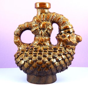 Könnte beinhalten: Eine braune Keramikvase mit einem einzigartigen, skurrilen Design. Die Vase ist in Form eines Vogels mit einem strukturierten, schuppigen Körper und einem langen, gebogenen Hals gestaltet.
