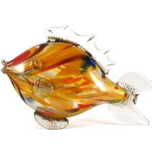 May include: A colorful glass fish figurine with a clear glass tail and fins. The body of the fish is made of clear glass with swirls of yellow, orange, red, and blue.