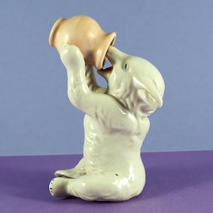 Puede incluir: Una figurita de cerámica blanca de un oso bebiendo de una jarra de cerámica rosa.