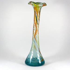 May include: A tall, clear glass vase with a swirling pattern of yellow, orange, and blue. The vase has a wide, flared opening and a narrow base.