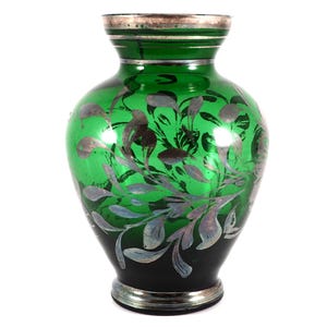 May include: A green glass vase with silver floral designs. The vase has a round body and a narrow neck.
