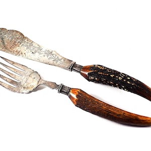 May include: A vintage silver knife and fork set with ornate handles made of dark brown stag horn.