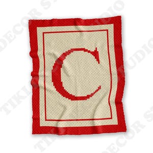 May include: A handmade crochet blanket featuring a large red letter "C" on a cream-colored background. The blanket has a red border and a square design. The blanket is a cozy home decor item.
