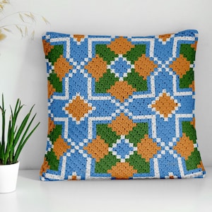 May include: A square decorative pillow with a geometric pattern. The design features a repeating pattern of blue, orange, green, and white squares and diamonds. The pillow is made of a soft, textured fabric.