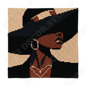 May include: A square needlepoint canvas featuring a stylized profile of a person with dark brown skin, wearing a wide-brimmed black hat and large hoop earrings. The design uses a geometric, pixelated aesthetic with a color palette of black, tan, and brown.