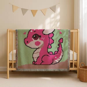 May include: A pink pixelated dragon blanket with a green background and brown fringe. The dragon has large eyes and is surrounded by small pink hearts. The blanket is draped over a wooden crib.