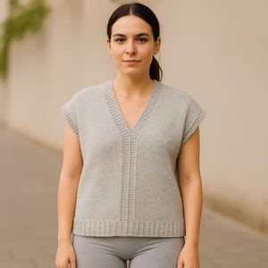 Peut inclure: Un pull sans manches gris clair avec un col en V. Le pull présente un ourlet côtelé et un motif en tricot texturé. Le modèle porte un legging gris. Une pièce polyvalente pour superposer.