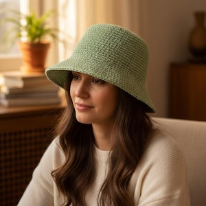 May include: A light green crochet bucket hat with a wide brim. The hat is made of a textured yarn and has a slightly flared shape. The hat is a soft, muted green color. The hat is a stylish accessory.
