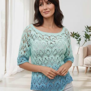 Op de afbeelding: Een lichtblauwe gehaakte top met een ronde hals en driekwart mouwen. De top heeft een gradiënteffect, dat overgaat van een lichtere tint aan de bovenkant naar een donkerdere blauwe kleur aan de onderkant. Het openwerkontwerp voegt een delicate, luchtige kwaliteit toe.