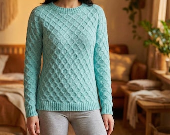 May include: A light blue sweater with a textured diamond pattern. The sweater has a crew neck and long sleeves. The bottom and cuffs have a ribbed design. The person is wearing gray shorts.