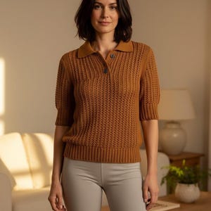 May include: A woman wearing a brown knit polo shirt with short sleeves and a button-down collar. She is also wearing gray biker shorts. The background includes a living room setting with a couch, table, and lamp.