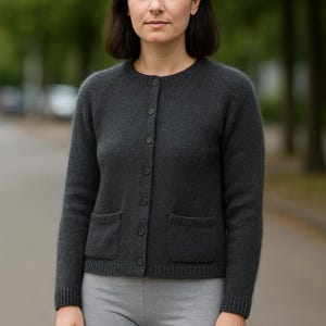 Puede incluir: Un cárdigan gris oscuro con cuello redondo, mangas largas y dos bolsillos delanteros. El suéter tiene cierre de botones y se combina con pantalones cortos grises. El estilo general es casual y cómodo.