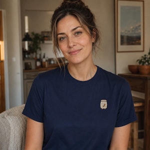 May include: A dark navy blue short-sleeved t-shirt featuring a small, centred graphic of a beige jar with a smiling face and a small spoon inside. The shirt has a classic crew neckline and rolled sleeves, providing a simple and clean appearance.