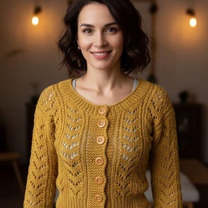 May include: Mustard yellow cardigan with a round neckline and wooden buttons. The knitted sweater features a detailed openwork pattern on the sleeves and front. The woman is wearing blue jeans.