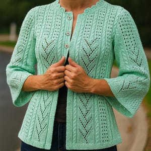 May include: A mint green, open-front cardigan with a scalloped neckline and three buttons. The knitted jacket features a textured pattern with a chevron design and three-quarter sleeves. The person is wearing dark blue jeans.