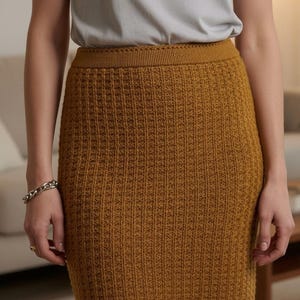 May include: Mustard-colored, knee-length skirt with a textured, ribbed knit pattern. The skirt has a fitted silhouette and a ribbed waistband. The model is wearing a gray t-shirt and a silver bracelet. The skirt is made of a soft, comfortable material.