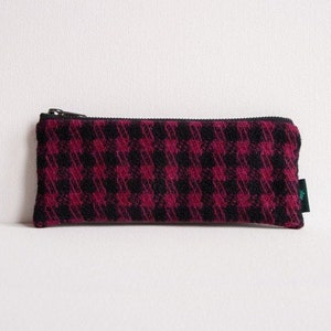 Op de afbeelding: Een rechthoekige etui met een zwarte ritssluiting en een pied-de-poule patroon in zwart en magenta. De etui is gemaakt van een textiel met textuur en heeft een klein groen label aan de zijkant.