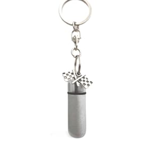 May include: Silver keychain with a small silver cylinder attached. The cylinder has a checkered flag design on the top and a black ring around the middle.