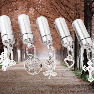 May include: Five silver cremation urns with different charms attached. The charms include a butterfly, a tree, a rose, a heart, and a cross.