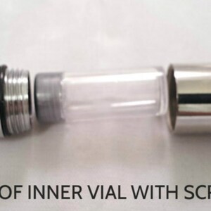 Pode incluir: Uma c&aacute;psula de porta-chaves em metal prateado com uma carca&ccedil;a exterior destac&aacute;vel e um frasco interior transparente. A tampa met&aacute;lica possui um mecanismo de rosca e um anel. O texto WATERPROOF INNER VIAL WITH SCREW-ON CAP &eacute; vis&iacute;vel.