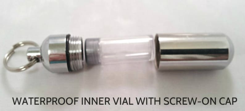 Pode incluir: Uma c&aacute;psula de porta-chaves em metal prateado com uma carca&ccedil;a exterior destac&aacute;vel e um frasco interior transparente. A tampa met&aacute;lica possui um mecanismo de rosca e um anel. O texto WATERPROOF INNER VIAL WITH SCREW-ON CAP &eacute; vis&iacute;vel.