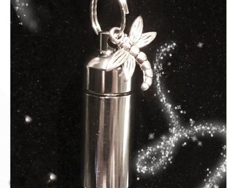 May include: A silver necklace with a small cylindrical pendant and a dragonfly charm. The pendant has a screw-on top and is likely used for holding ashes or other small mementos.