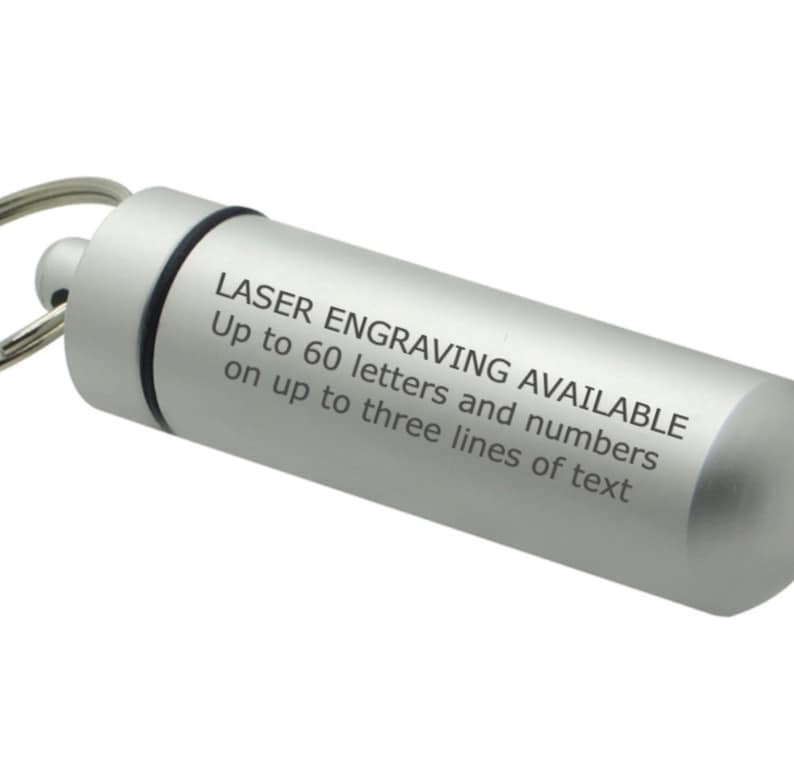 Pode incluir: Um porta-chaves cil&iacute;ndrico de metal prateado com tampa de rosca e argola de metal. A lateral do recipiente apresenta um texto impresso a preto que diz: LASER ENGRAVING AVAILABLE Up to 60 letters and numbers on up to three lines of text.