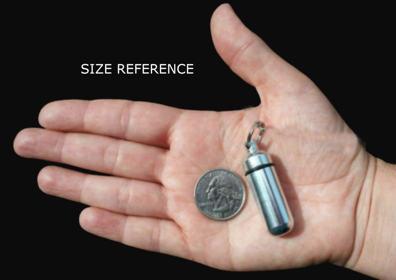 Pode incluir: Um pequeno recipiente cil&iacute;ndrico para comprimidos em metal prateado com um anel de veda&ccedil;&atilde;o de borracha preta e um anel de fixa&ccedil;&atilde;o met&aacute;lico no topo. O recipiente &eacute; mostrado ao lado de uma moeda como refer&ecirc;ncia de tamanho.