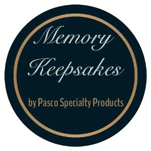 May include: A dark blue circle with a gold border. The text "Memory Keepsakes" is written in a cursive font in light blue. The text "by Pasco Specialty Products" is written in white below the cursive text.