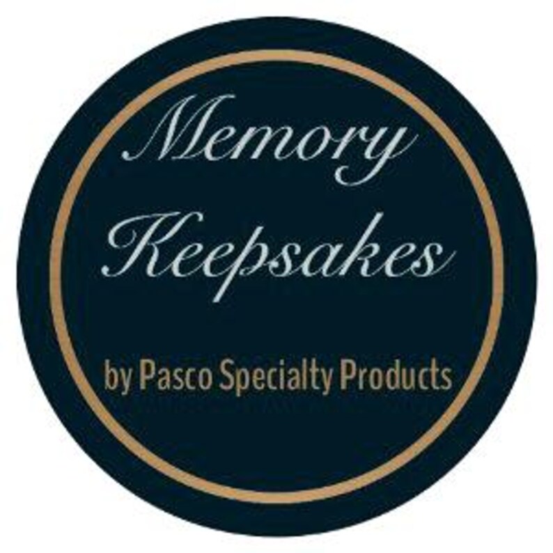 May include: A dark blue circle with a gold border. The text "Memory Keepsakes" is written in a cursive font in light blue. The text "by Pasco Specialty Products" is written in white below the cursive text.