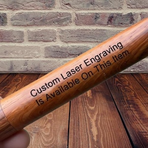 May include: A cylindrical wooden object with a polished brown grain finish. The surface features dark, laser-engraved text that reads: Custom Laser Engraving Is Available On This Item. The wood displays natural light and dark brown patterns.