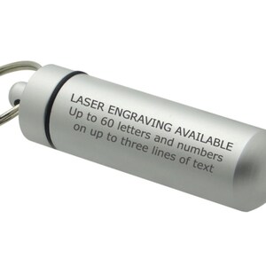May include: A silver-colored, cylindrical keychain pendant. The pendant has a screw-on top and a keyring attachment. Text on the side reads: "LASER ENGRAVING AVAILABLE Up to 60 letters and numbers on up to three lines of text."