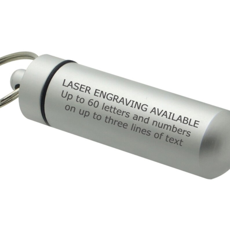 May include: A silver-colored, cylindrical keychain pendant. The pendant has a screw-on top and a keyring attachment. Text on the side reads: "LASER ENGRAVING AVAILABLE Up to 60 letters and numbers on up to three lines of text."