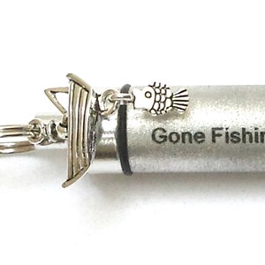May include: Silver necklace with a small silver boat charm and a fish charm. The pendant is a silver cylinder with the words "Gone Fishin'" engraved on it.