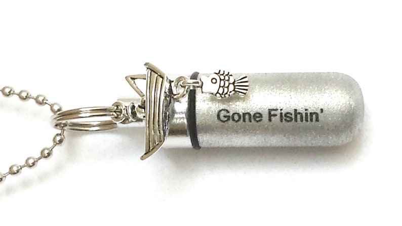 May include: Silver necklace with a small silver boat charm and a fish charm. The pendant is a silver cylinder with the words "Gone Fishin'" engraved on it.