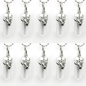 May include: A collection of silver-colored pendant necklaces. Each pendant features a cylindrical design with a hand gesture, attached to a ball chain. The pendants are displayed against a white background.