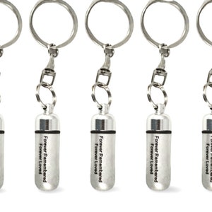 May include: Five silver keychains with small cylindrical containers attached. Each container has the text "Forever Remembered Forever Loved" engraved on it.