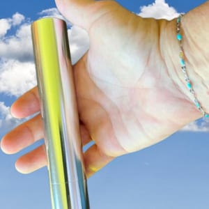 May include: A cylindrical metal tube with a polished, reflective silver finish. The object has a smooth, seamless exterior surface and a straight, uniform shape. The metal reflects light, creating bright highlights along its length.