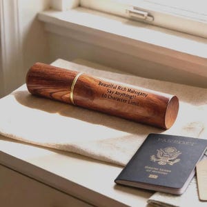 May include: A cylindrical mahogany wood case with a gold-colored metal band and the engraved text: Beautiful Rich Mahogany, Say Anything!!, 60 Character Limit. Next to the case is a dark blue United States passport with a gold emblem.