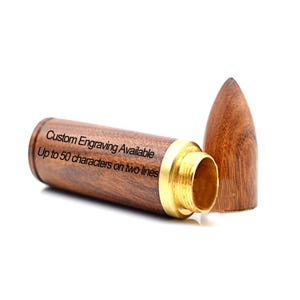 May include: A wooden bullet-shaped container with a gold-colored metal rim and a separate, pointed wooden cap. The container has text that reads "Custom Engraving Available Up to 50 characters on two lines."