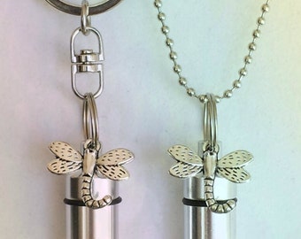 May include: Two silver tone cremation urns with dragonfly charms. One urn is attached to a silver key chain and the other is attached to a silver chain.