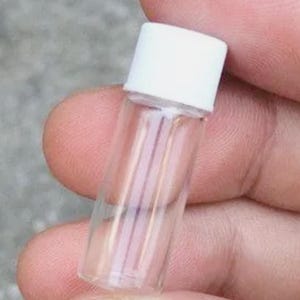 Pode incluir: Um pequeno frasco de vidro transparente com corpo cil&iacute;ndrico e uma tampa de rosca branca s&oacute;lida. O recipiente &eacute; transparente, permitindo uma vis&atilde;o clara do espa&ccedil;o interior, e possui uma estrutura simples e funcional para armazenamento.