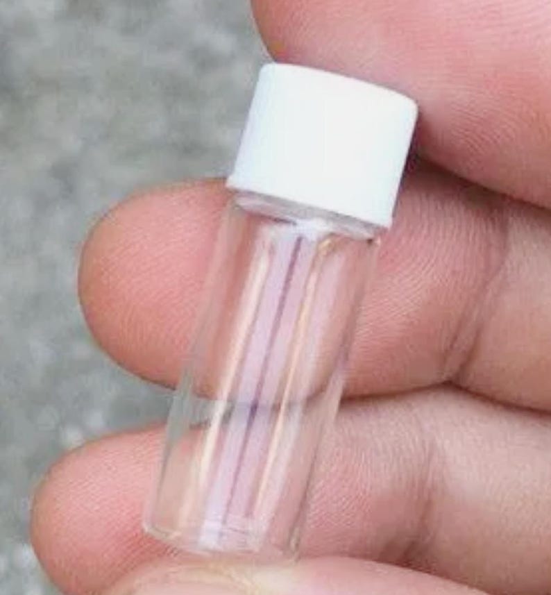 Pode incluir: Um pequeno frasco de vidro transparente com corpo cil&iacute;ndrico e uma tampa de rosca branca s&oacute;lida. O recipiente &eacute; transparente, permitindo uma vis&atilde;o clara do espa&ccedil;o interior, e possui uma estrutura simples e funcional para armazenamento.
